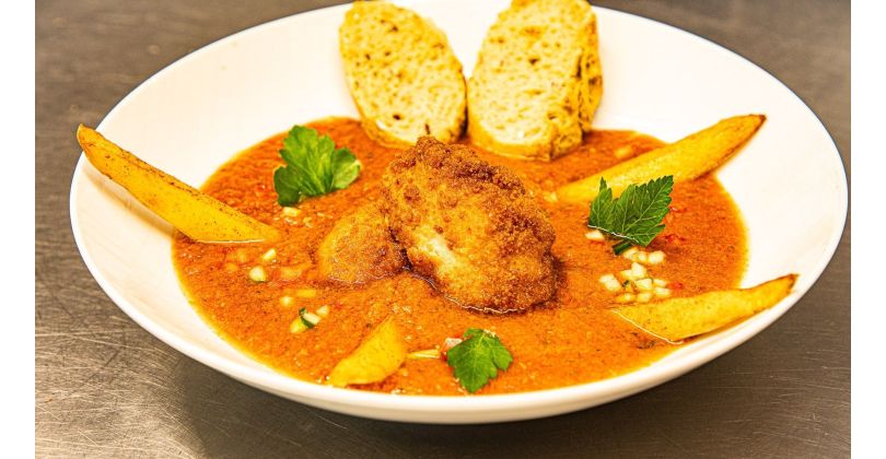 Crispy fried bull testicles with fried potato wedges on fresh gazpacho